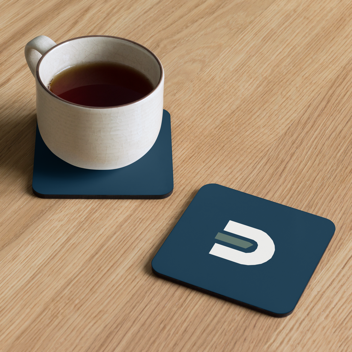 Mug on a navy Dads in the Game D emblem coaster beside a second coaster on a wooden table