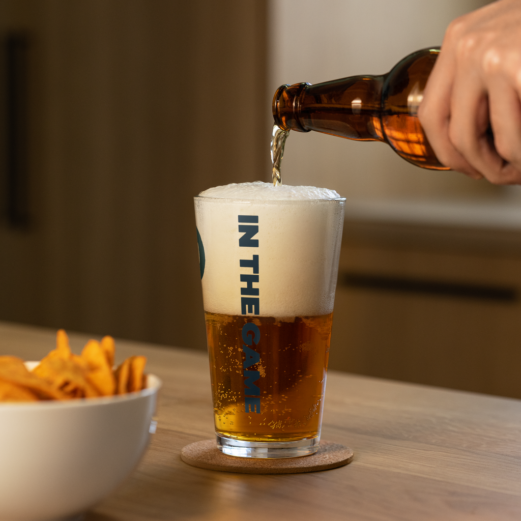 Beer being poured into a Dads in the Game pint glass with vertical In the Game lettering facing forward