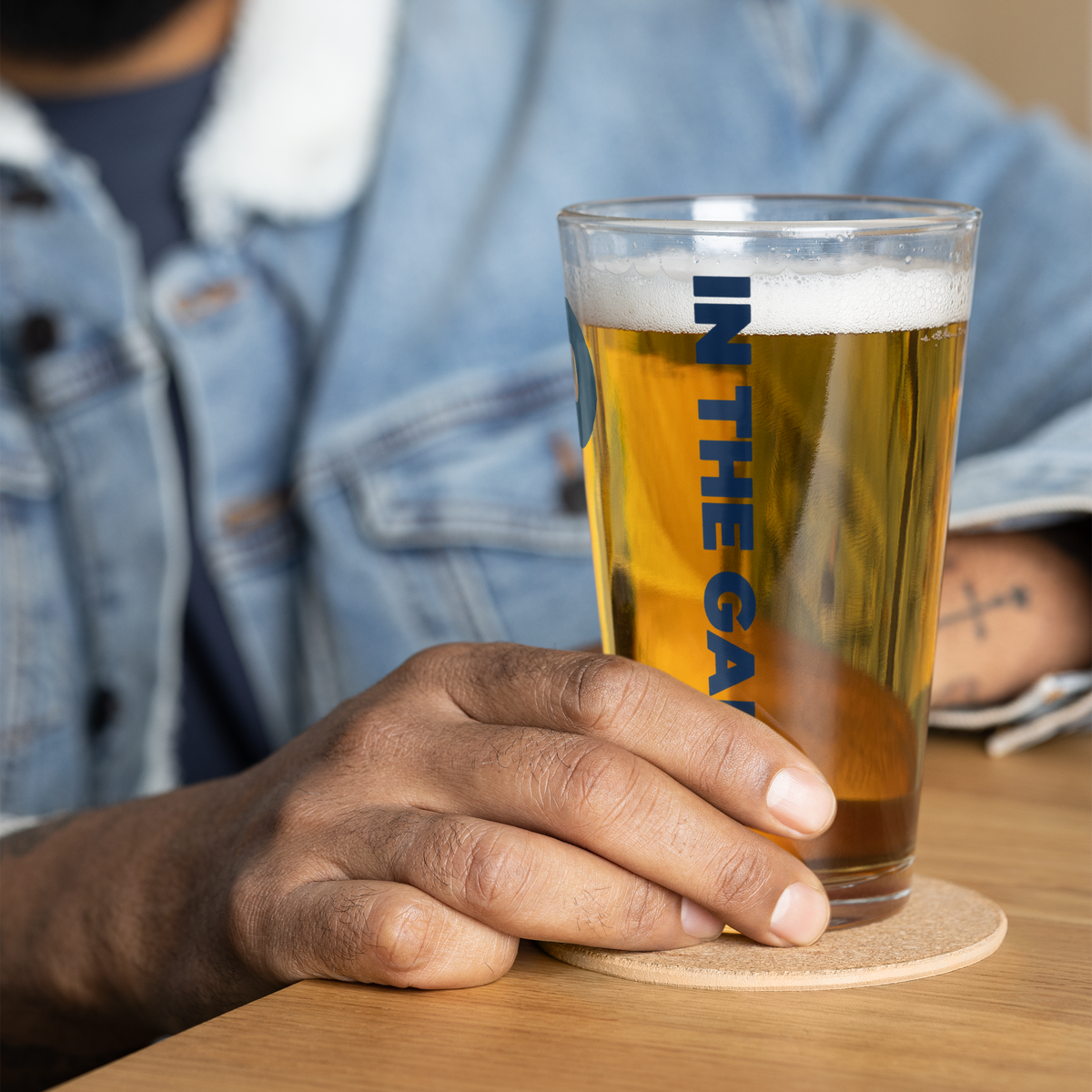 Person holding a filled Dads in the Game pint glass with vertical In the Game lettering
